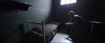 Movie still from “A Hidden Life” (2019), directed by Terrence Malick – A man sitting on a chair next to a bed in a room; Wide shot, High angle