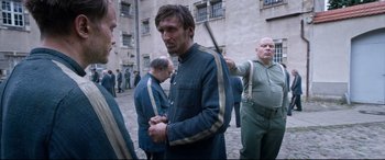 Movie still from “A Hidden Life” (2019), directed by Terrence Malick – A group of men standing next to each other on a street; Medium shot, Over the shoulder angle