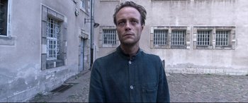 Movie still from “A Hidden Life” (2019), directed by Terrence Malick – A man standing in front of a building; Close Up shot, Low angle