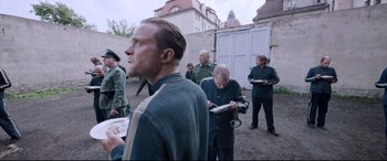 Movie still from “A Hidden Life” (2019), directed by Terrence Malick – A group of men standing next to each other on a street; Medium shot, Over the shoulder angle