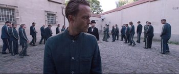 Movie still from “A Hidden Life” (2019), directed by Terrence Malick – A group of men standing in a courtyard with buildings in the background; Medium shot, Over the shoulder angle