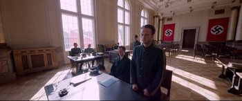 Movie still from “A Hidden Life” (2019), directed by Terrence Malick – A man sitting at a table in front of two other men; Wide shot, High angle