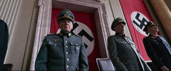Movie still from “A Hidden Life” (2019), directed by Terrence Malick – Two men in military uniforms stand in front of a nazi flag; Medium shot, Low angle