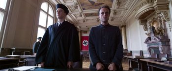 Movie still from “A Hidden Life” (2019), directed by Terrence Malick – Two men standing in front of a nazi flag; Medium shot, Low angle