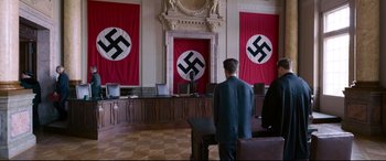 Movie still from “A Hidden Life” (2019), directed by Terrence Malick – A man standing in front of a podium in front of three nazi flags; Wide shot, High angle