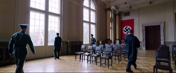 Movie still from “A Hidden Life” (2019), directed by Terrence Malick – Two men are standing in front of chairs in an empty room; Extreme Wide shot, High angle
