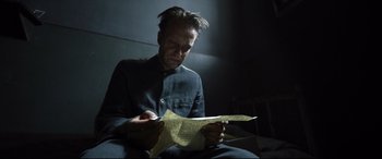 Movie still from “A Hidden Life” (2019), directed by Terrence Malick – A man sitting in the dark looking at a piece of paper; Medium shot, High angle