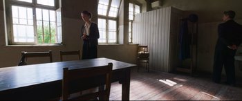 Movie still from “A Hidden Life” (2019), directed by Terrence Malick – A woman standing next to a table in a room; Wide shot, Over the shoulder angle