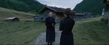 Movie still from “A Hidden Life” (2019), directed by Terrence Malick – Two women are standing in front of a log cabin; Wide shot, Over the shoulder angle