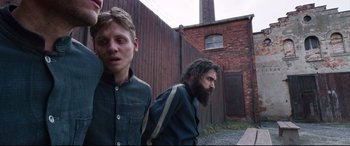 Movie still from “A Hidden Life” (2019), directed by Terrence Malick – Two men standing next to each other in front of a brick building; Medium shot, Over the shoulder angle