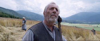 Movie still from “A Hidden Life” (2019), directed by Terrence Malick – An older man holding a hammer in a grassy field; Close Up shot, Low angle