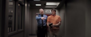 Movie still from “Escape Plan” (2013), directed by Mikael Håfström – A man in an orange t - shirt is standing next to a man in an orange t - shirt; Medium shot, Low angle