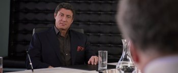 Movie still from “Escape Plan” (2013), directed by Mikael Håfström – A man sitting at a table with a glass in front of him; Medium shot, Over the shoulder angle