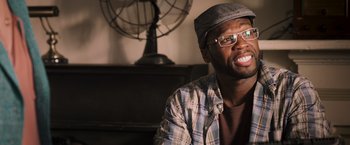 Movie still from “Escape Plan” (2013), directed by Mikael Håfström – A man wearing glasses and a hat sitting in front of a clock; Close Up shot, Over the shoulder angle