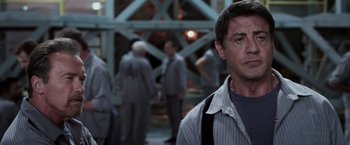 Movie still from “Escape Plan” (2013), directed by Mikael Håfström – A man standing in front of a group of people; Close Up shot, Over the shoulder angle