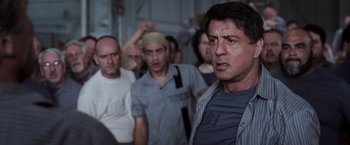 Movie still from “Escape Plan” (2013), directed by Mikael Håfström – A group of people standing around a building; Close Up shot, Low angle