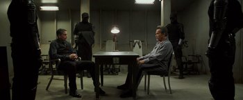 Movie still from “Escape Plan” (2013), directed by Mikael Håfström – A group of men sitting at a table in an interrogation room; Wide shot, Over the shoulder angle