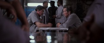 Movie still from “Escape Plan” (2013), directed by Mikael Håfström – A couple of men sitting next to each other at a table; Medium shot, Over the shoulder angle