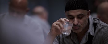 Movie still from “Escape Plan” (2013), directed by Mikael Håfström – A man holding a glass of water in his hand; Close Up shot, Over the shoulder angle