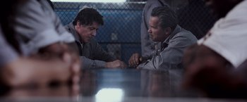 Movie still from “Escape Plan” (2013), directed by Mikael Håfström – Two men arm wrestling at a table in front of a chain link fence; Medium shot, Over the shoulder angle