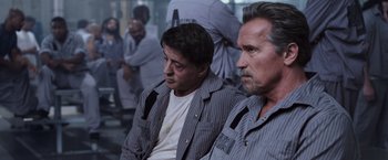 Movie still from “Escape Plan” (2013), directed by Mikael Håfström – A couple of men sitting next to each other; Medium shot, Low angle