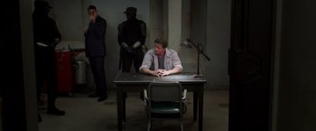 Movie still from “Escape Plan” (2013), directed by Mikael Håfström – A man sitting at a table in front of two other men; Wide shot, Over the shoulder angle