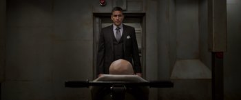 Movie still from “Escape Plan” (2013), directed by Mikael Håfström – A man in a suit and tie standing in front of a bed; Medium shot, Low angle
