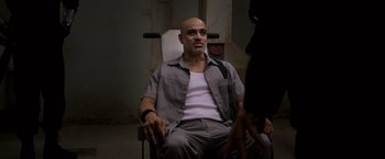 Movie still from “Escape Plan” (2013), directed by Mikael Håfström – A bald man sitting in a chair in a room; Medium shot, High angle
