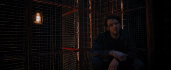 Movie still from “Escape Room: Tournament of Champions” (2021), directed by Adam Robitel – A man leaning against a metal fence; Medium shot, Low angle