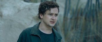 Movie still from “Escape Room: Tournament of Champions” (2021), directed by Adam Robitel – A young man with curly brown hair wearing a black shirt; Close Up shot, Over the shoulder angle