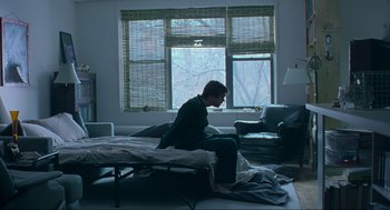 Movie still from “Eternal Sunshine of the Spotless Mind” (2004), directed by Michel Gondry – A man sitting on top of a bed in front of a window; Wide shot, High angle