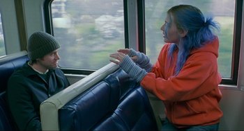 Movie still from “Eternal Sunshine of the Spotless Mind” (2004), directed by Michel Gondry – Two people sitting on a train looking at each other; Medium shot, Over the shoulder angle