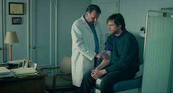 Movie still from “Eternal Sunshine of the Spotless Mind” (2004), directed by Michel Gondry – A doctor examines a man's arm in a room; Medium shot, Over the shoulder angle