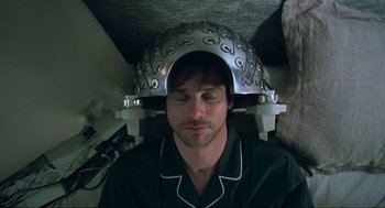 Movie still from “Eternal Sunshine of the Spotless Mind” (2004), directed by Michel Gondry – A man with a helmet on his head is laying down; Close Up shot, Overhead angle