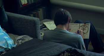 Movie still from “Eternal Sunshine of the Spotless Mind” (2004), directed by Michel Gondry – A man sitting on a couch writing on a piece of paper; Medium shot, Over the shoulder angle