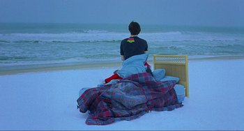 Movie still from “Eternal Sunshine of the Spotless Mind” (2004), directed by Michel Gondry – A man sitting on a blanket on the beach by the water; Wide shot, High angle