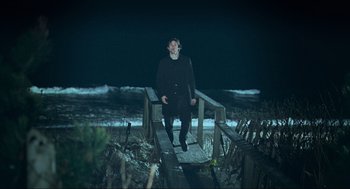 Movie still from “Eternal Sunshine of the Spotless Mind” (2004), directed by Michel Gondry – A man standing on a wooden bridge near the ocean at night; Wide shot, High angle