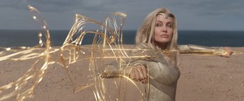 Movie still from “Eternals” (2021), directed by Chloé Zhao – A woman in a white dress holding a sword on the beach; Medium shot, Low angle