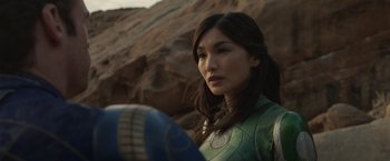 Movie still from “Eternals” (2021), directed by Chloé Zhao – A woman in a green costume holding a blue object; Close Up shot, Over the shoulder angle