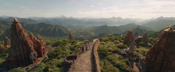 Movie still from “Eternals” (2021), directed by Chloé Zhao – A group of people walking on a path near a mountain; Extreme Wide shot, High angle