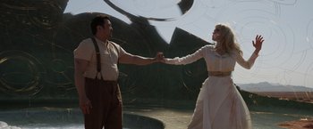 Movie still from “Eternals” (2021), directed by Chloé Zhao – A man and a woman holding hands while standing next to each other; Medium shot, Low angle