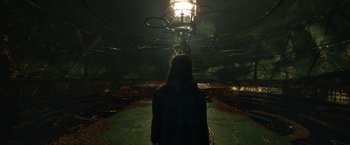 Movie still from “Eternals” (2021), directed by Chloé Zhao – A woman is standing in a dark room; Wide shot, Low angle