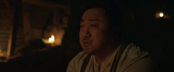 Movie still from “Eternals” (2021), directed by Chloé Zhao – A man with a mustache sitting in a dimly - lit room; Close Up shot, Over the shoulder angle