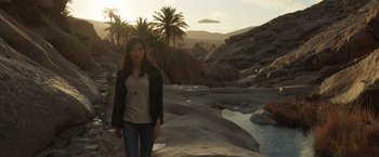 Movie still from “Eternals” (2021), directed by Chloé Zhao – A woman standing on a rocky shore near a body of water; Wide shot, High angle