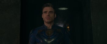 Movie still from “Eternals” (2021), directed by Chloé Zhao – A man in a blue and gold jacket looking at the camera; Close Up shot, Over the shoulder angle