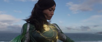 Movie still from “Eternals” (2021), directed by Chloé Zhao – A woman in a green and yellow outfit with a light in her body; Medium shot, Over the shoulder angle