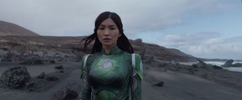 Movie still from “Eternals” (2021), directed by Chloé Zhao – A woman in a green and silver costume standing on a beach; Medium shot, Low angle