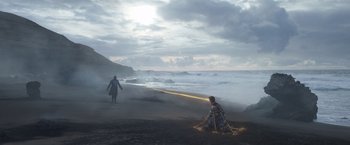 Movie still from “Eternals” (2021), directed by Chloé Zhao – A person is sitting on the beach with a flashlight; Extreme Wide shot, Low angle