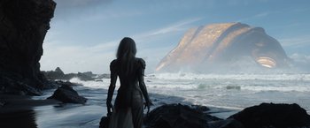 Movie still from “Eternals” (2021), directed by Chloé Zhao – A woman standing on a rock near the ocean; Extreme Wide shot, Over the shoulder angle