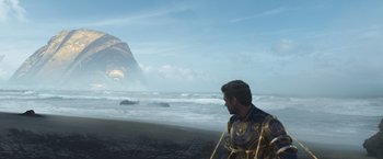 Movie still from “Eternals” (2021), directed by Chloé Zhao – A man standing on a beach near the ocean; Extreme Wide shot, Over the shoulder angle